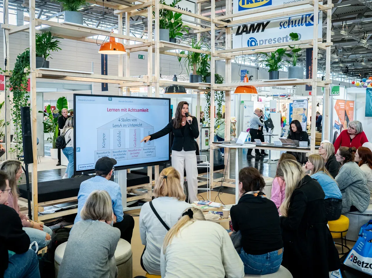 Eine Frau hält einen Vortrag vor Publikum auf einer Messe.